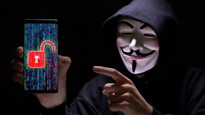 Minh họa về một người mang mặt nạ hacker Anonymous cầm chiếc smartphone đã bị hack. Ảnh: Phonebuff/YouTube