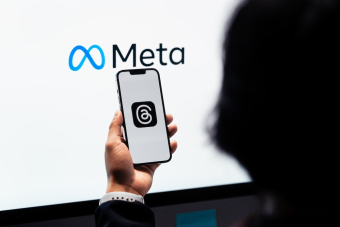 Logo Threads hiển thị trên một mẫu smartphone của người dùng, phía sau là logo Meta. Ảnh: Unsplash